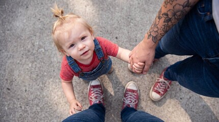 Naklejka premium Overhead view of toddler holding hands with two tattooed parents outdoors