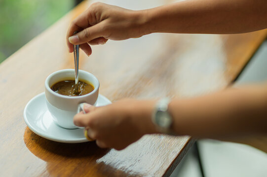 Close-Up of Hands Stirring Coffee in White Ceramic Cup