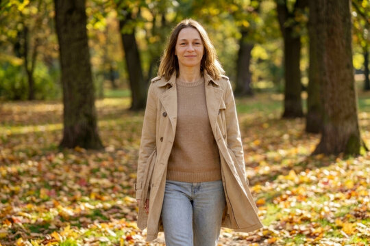 Happy woman walking through autumn park with golden leaves representing peace mindfulness and wellness