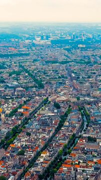 Vertical video. Amsterdam, Netherlands. Panoramic aerial sweep over the 17th-century canal belt and Amstel River locks, dense historic rooftops and waterways under soft overcast morning light. Drone 