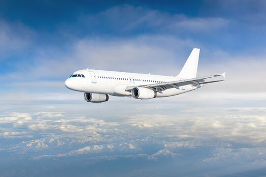 White modern airplane flying in the air over snow covered mountains