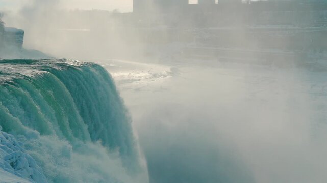 An approaching shot highlights turquoise water crashing forcefully into the winter falls