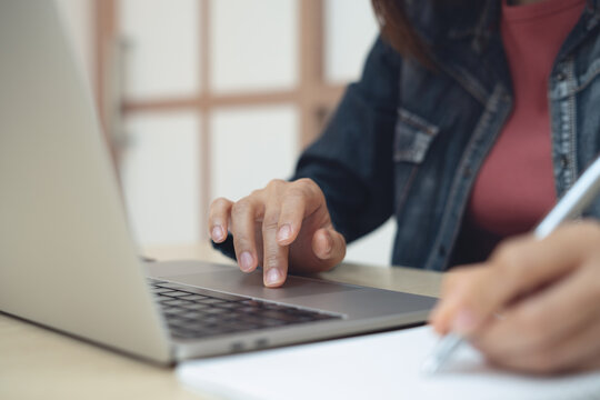 Woman working on laptop searching the information and writing in notebook, online studying, remote work, business planning