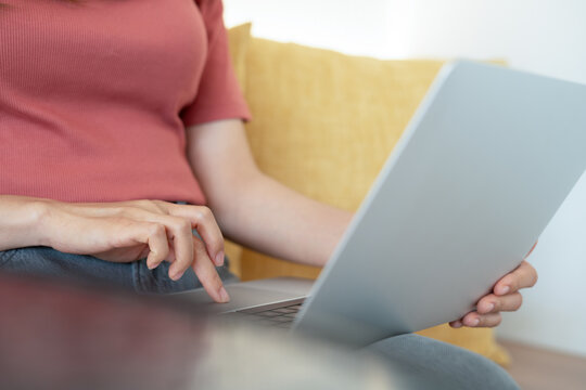 Woman sitting on sofa using laptop on her lap, working at at home, surfing the net, doing online e-commerce shopping, 