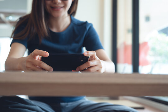 Young  asian woman watching video or tv program on smartphone or enjoying playing video game at home 