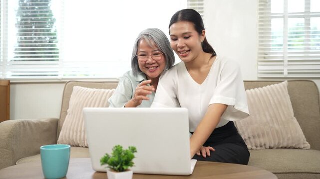 Senior woman and young caregiver using a laptop together at home, promoting digital inclusion, family support, and elderly technology learning.