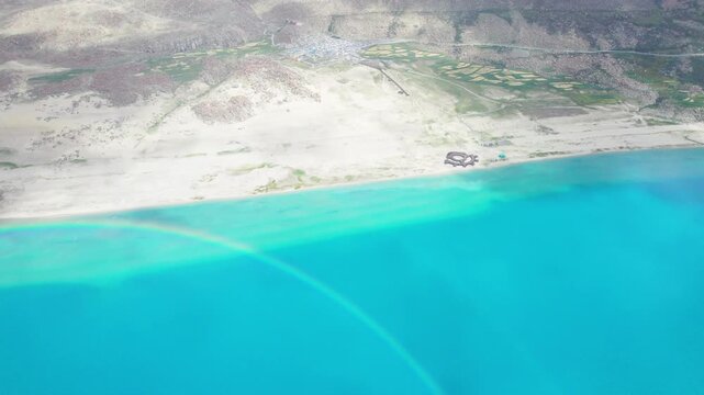 Drone view of Pegu Tso lake or Peikucuo in sunny and rainy day in Shigatse, Tibet, China, beautiful twin rainbows over peaceful turquoise sea in Xizang, 4k real time footage travel concept