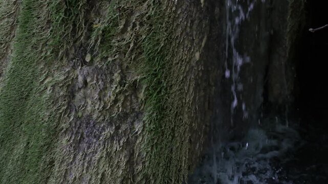 Close-up dark, wet video of Tufa Formation and calcifying moss Les Cascades de Rivert. UNESCO Global Geopark Or&iacute;gens. Details of splashes and mineral deposits. Minimal. Copy space. Documentary video.
