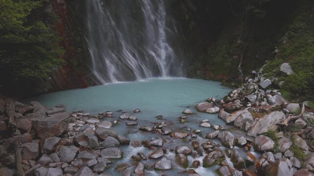 Waterfall flows into milky natural hot spring pool in forested mountain - Kagoshima, Japan
