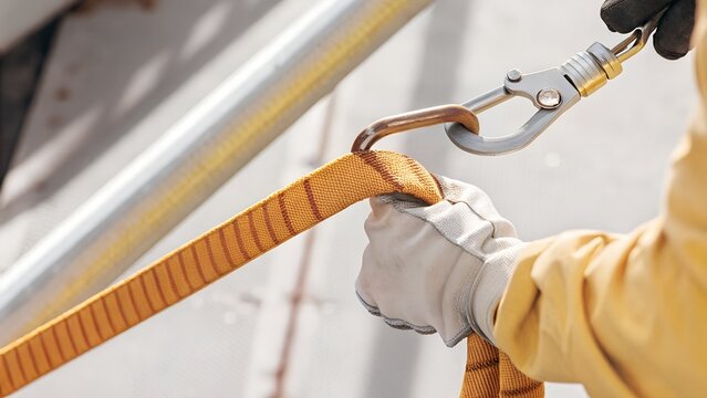 Close-up of a construction worker securely attaching a fall protection safety lanyard hook before working at height, emphasizing workplace safety, PPE compliance, and industrial safety standards.