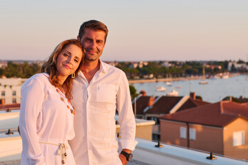 Obraz premium Mature Couple Relaxing on Rooftop Balcony With Sea View at Sunset in Coastal Town