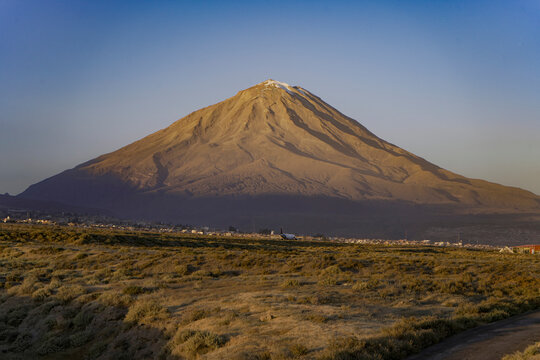 El Misti volcano glows with golden light at sunset as a plane takes off over Arequipa