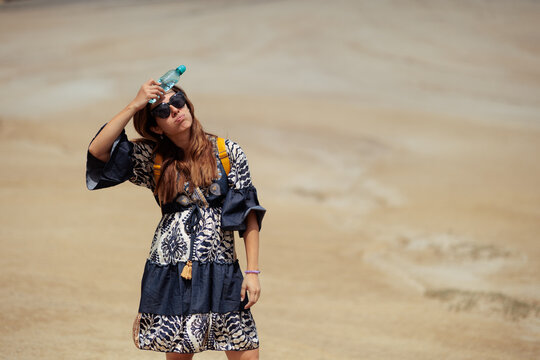 Exhausted Woman Holding Cold Water Bottle To Her Face In Hot Desert. Overheated female traveler tries to cool down during a scorching summer trek