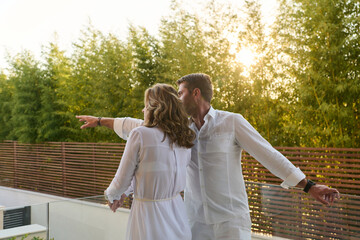 Obraz premium Couple On Home Balcony At Sunset Pointing Over Rooftop Terrace With Relaxed Romantic Vibe