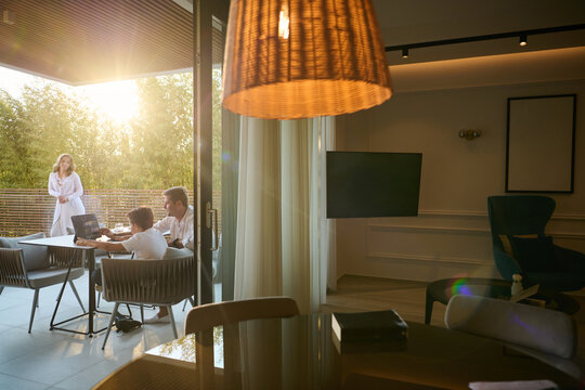 Family Working and Relaxing on a Modern Home Balcony at Sunset With Laptop and Conversation