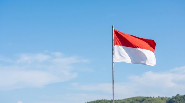 The national flag of Indonesia waving against a clear blue sky. A patriotic symbol representing national identity, independence, freedom, and pride with ample copy space