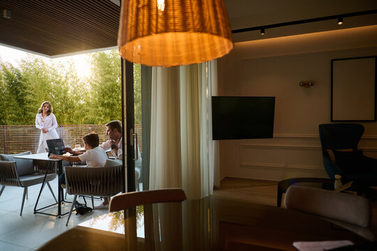 Family Working and Relaxing on a Modern Home Balcony Terrace Overlooking Greenery at Sunset