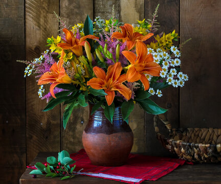 still life with daylily and daisies in a clay pot on a dark background. garden flowers on a wooden table.