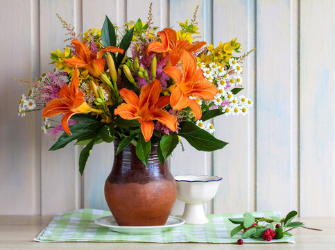 light still life with lilies and daisies on a table in a cottage. garden flowers in a jug by a wooden wall.