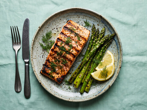 Grilled salmon fillet with roasted asparagus and lemon slices top view.