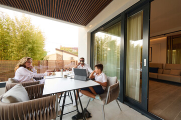 Naklejka premium Family Working and Relaxing on a Home Balcony Terrace With Laptop, Coffee and Casual Conversation