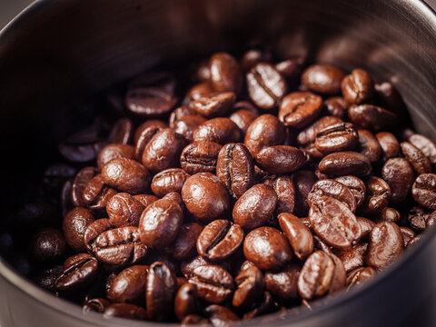 Close-up of freshly roasted coffee beans inside a coffee grinder hopper. Rich texture and aroma for espresso concept