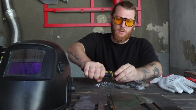 Worker sitting at workbench cutting steel rod into small pieces with nippers tool