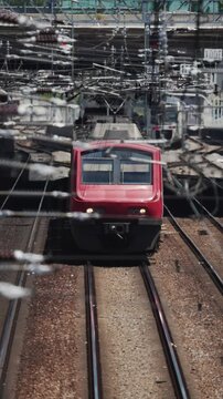 Train arrives at the station on a sunny day in a busy urban area with overhead wires and tracks