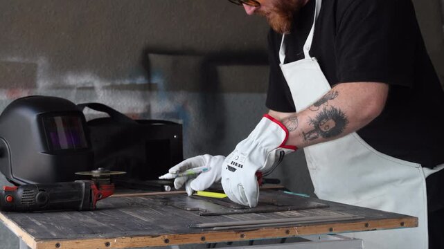 Worker hands in white safety gloves measuring metal plate on workshop bench