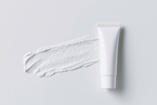 Overhead flat lay of an unlabelled white cosmetic cream tube beside a smooth white cream smear on a light gray background for skincare product presentation