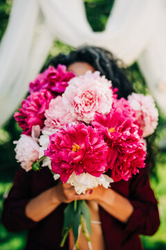 Woman hiding her face behind a lush peony bouquet