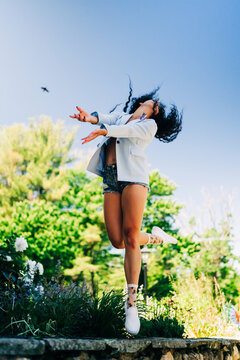 Joyful woman with curly hair leaps into the blue sky