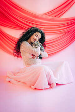 Elegant woman in pink dress lovingly cuddling a cat