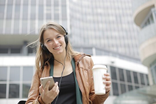 Smiling woman walking in city with coffee and music