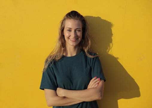 Happy young woman smiling by a bright yellow wall