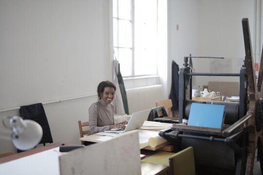 Smiling woman works on laptop in creative studio