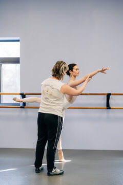 Ballet teacher guiding young ballerina during pose training