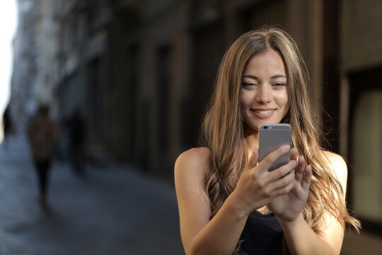 Smiling young woman looking at her smartphone on a city street