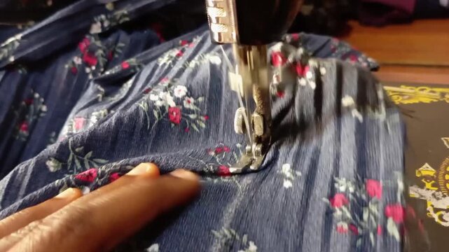African sewing navy blue floral fabric with sewing machine in action. Close up of hands of working dressmaker. Macro of blue black garment, adjusting, guiding. Home business tailor at work. Line drawn