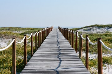 Fototapeta premium Wooden boardwalk leads over sand dunes toward the ocean horizon