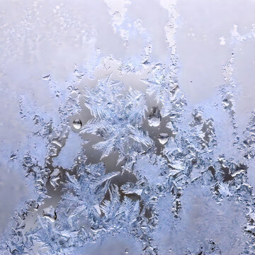 Detailed frost patterns on window glass with water droplets in cold morning light.