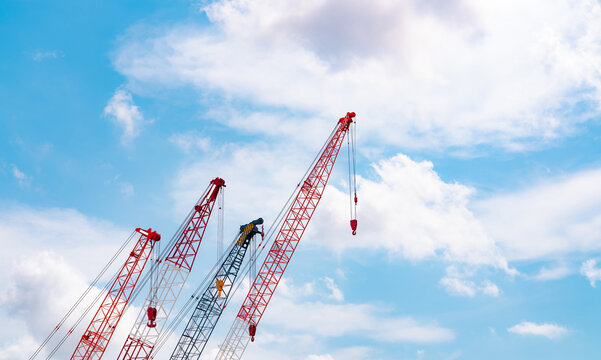 Crawler crane against blue sky and white clouds. Real estate industry. Red crawler crane use reel lift up equipment in construction site. Crane for rent. Crane dealership for construction business.