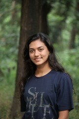 Naklejka premium Beautiful Bangladeshi girl with long open hair looking at camera standing near tree trunks outdoors