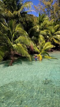 An Asian woman visits the tranquil shores of Koh Kood, Thailand, where clear waters gently lap against sandy beaches. Lush palm trees sway in the warm breeze as nature's beauty unfolds.