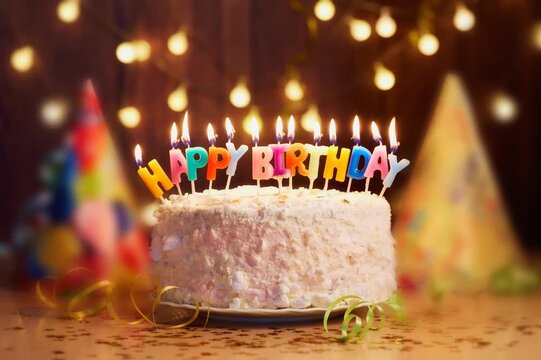 Festive birthday cake with colorful burning candles, party hats and glowing lights, creating a joyful celebration atmosphere for a special occasion.
