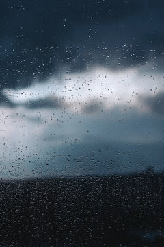 Raindrops dance elegantly on a window while dark clouds loom ominously above the horizon during a stormy evening
