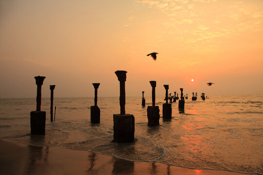 Sunset over the weathered remains of the old pier at Kozhikode Beach, Kerala, India, with waves washing around the concrete pillars