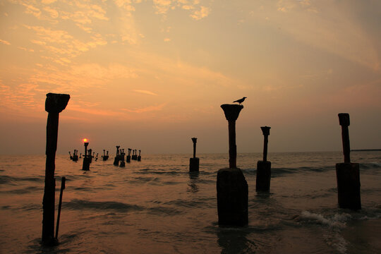Sunset over the weathered remains of the old pier at Kozhikode Beach, Kerala, India, with waves washing around the concrete pillars