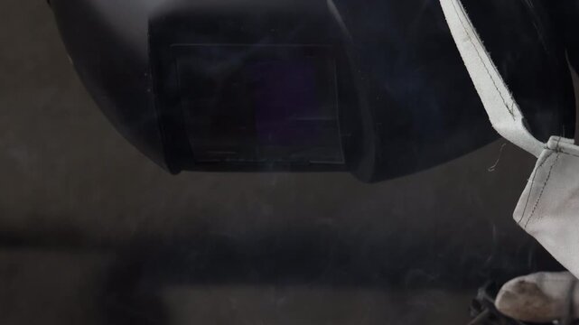 Selective focus on welder with helmet working on metal workpiece with bright sparks flying