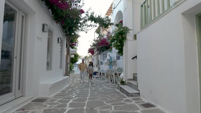A couple strolls through picturesque alleyways in Paros, Greece, as visitors enjoy the beauty of Cyclades. Vibrant flowers and local architecture create a perfect backdrop for unforgettable memories.